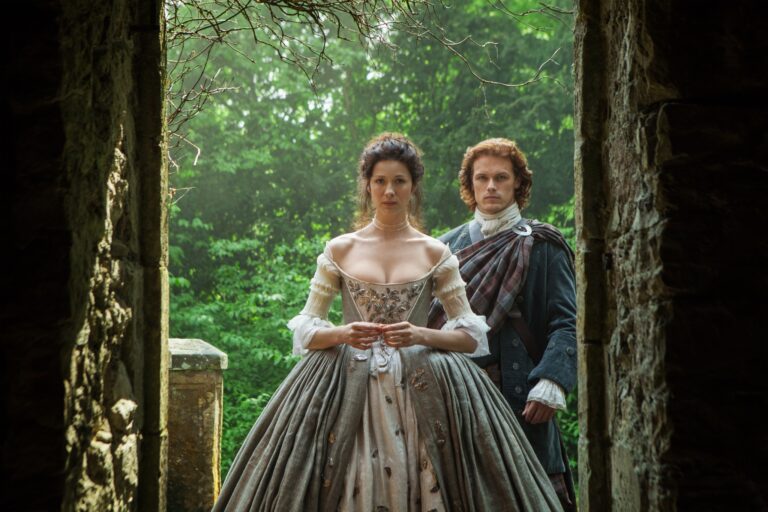 Claire and Jamie Fraser standing together in a stone doorway surrounded by greenery – still from Outlander (© 2014 Sony Pictures Television Inc.)